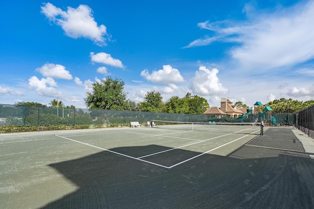 view of tennis court featuring playground community and fence