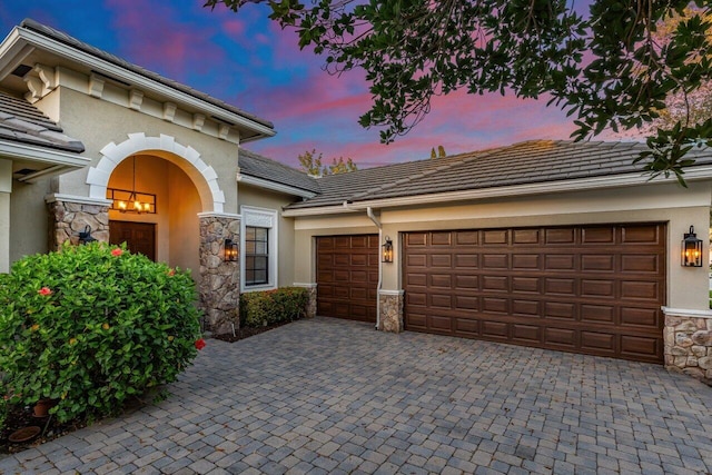 mediterranean / spanish-style house with decorative driveway, a tile roof, stucco siding, a garage, and stone siding