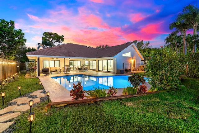 pool at dusk with a fenced in pool, a ceiling fan, a fenced backyard, a yard, and a patio area