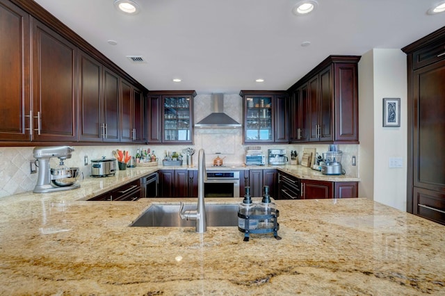 kitchen featuring visible vents, glass insert cabinets, light stone countertops, beverage cooler, and wall chimney exhaust hood