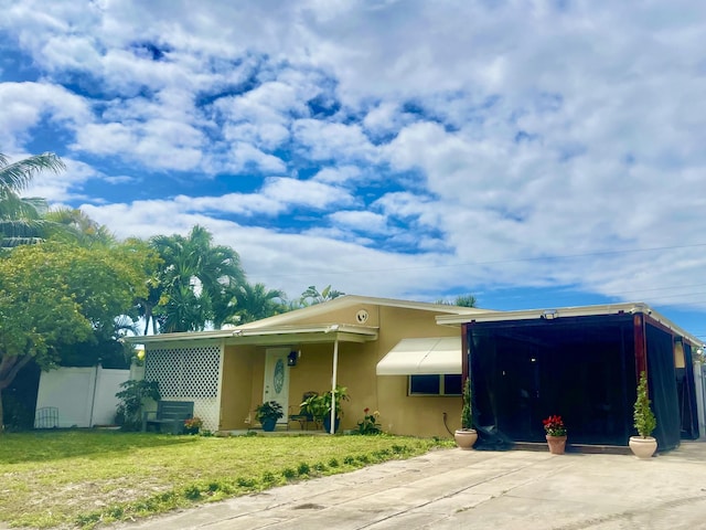 ranch-style house with concrete driveway, a front lawn, fence, and stucco siding