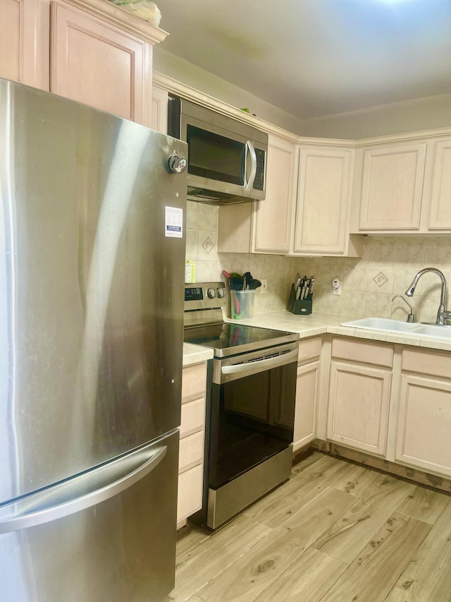 kitchen featuring appliances with stainless steel finishes, a sink, light wood finished floors, and decorative backsplash