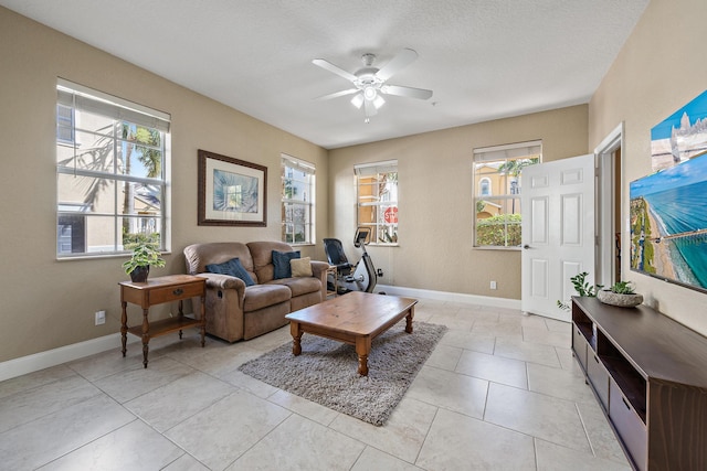 living area featuring ceiling fan, a textured ceiling, baseboards, and light tile patterned floors