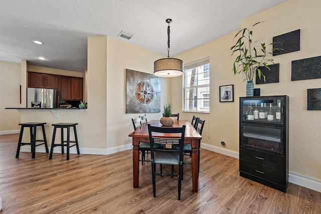 dining space featuring light wood-type flooring, baseboards, visible vents, and a textured ceiling