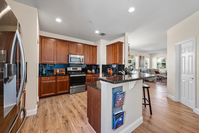 kitchen with visible vents, a kitchen breakfast bar, a peninsula, stainless steel appliances, and light wood-style floors