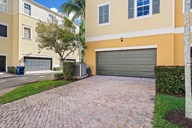 view of front of house with a garage, decorative driveway, cooling unit, and stucco siding