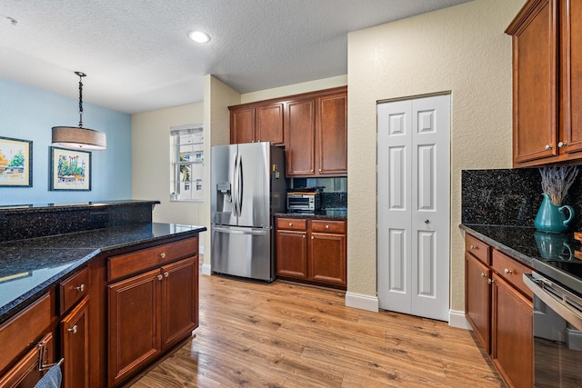 kitchen featuring a textured ceiling, light wood-style flooring, hanging light fixtures, stainless steel fridge with ice dispenser, and dark stone countertops