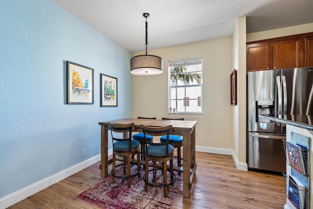 dining space with a textured ceiling, baseboards, and wood finished floors