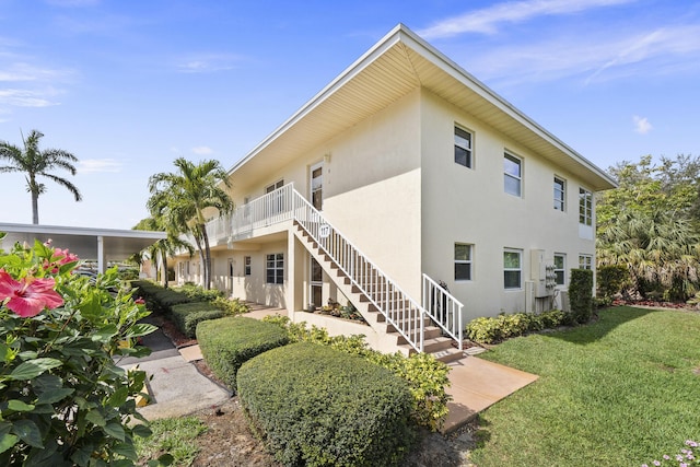 exterior space with stairway, a lawn, and stucco siding