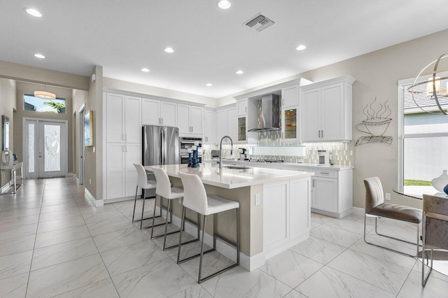 kitchen with freestanding refrigerator, a healthy amount of sunlight, a sink, and wall chimney exhaust hood