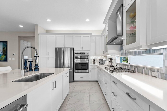 kitchen featuring tasteful backsplash, wall chimney exhaust hood, appliances with stainless steel finishes, marble finish floor, and a sink