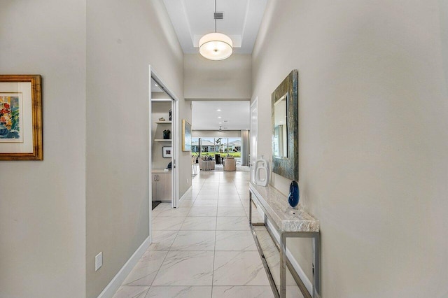 corridor with marble finish floor, a towering ceiling, and baseboards