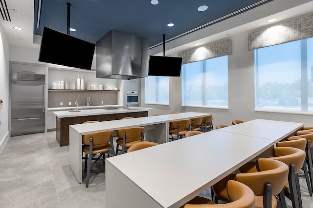 kitchen featuring extractor fan, stainless steel appliances, decorative backsplash, an island with sink, and a kitchen bar