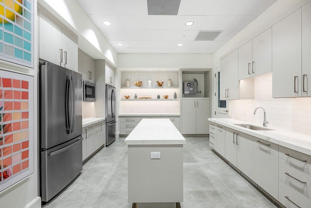 kitchen featuring a sink, appliances with stainless steel finishes, light stone countertops, open shelves, and tasteful backsplash