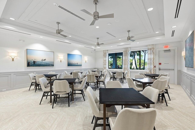 dining space with a wainscoted wall, crown molding, a raised ceiling, a decorative wall, and light carpet