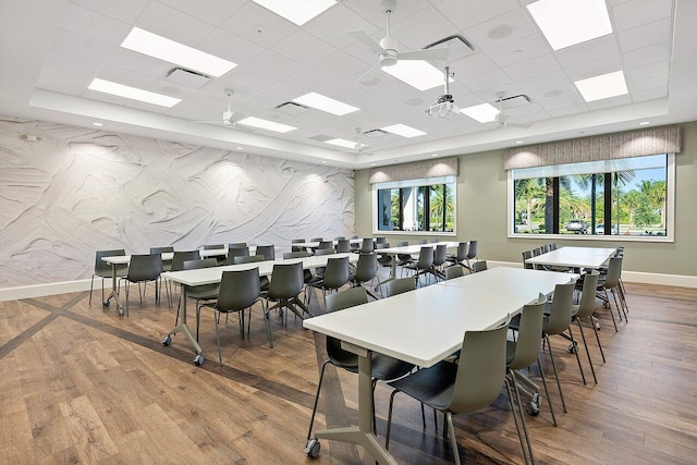 dining space with a tray ceiling, wood finished floors, visible vents, and baseboards