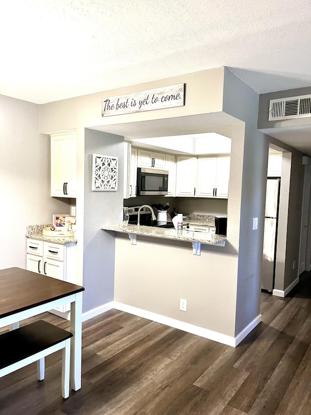 1548 SE Royal Green Cir Unit 105, Port Saint Lucie, FL 34952 - kitchen featuring stainless steel appliances, dark wood-style floors, white cabinetry, baseboards, and light stone counters