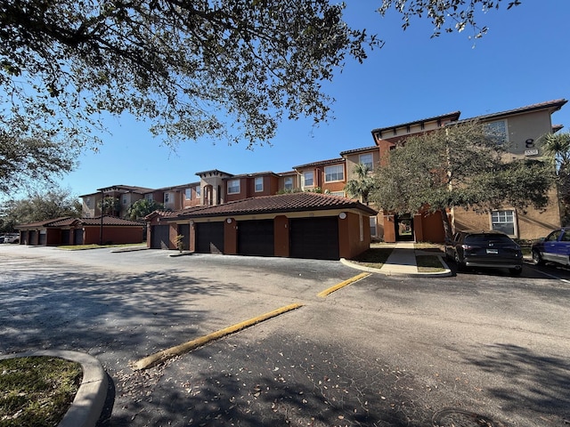 view of property featuring a tiled roof, stucco siding, a residential view, and community garages