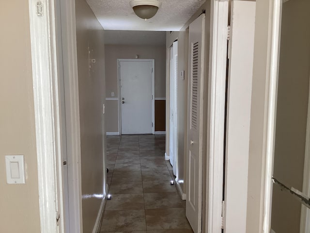 hall featuring baseboards, a textured ceiling, and tile patterned floors