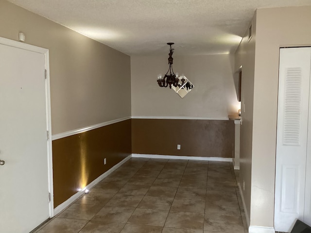 unfurnished dining area featuring an inviting chandelier, tile patterned flooring, baseboards, and a textured ceiling