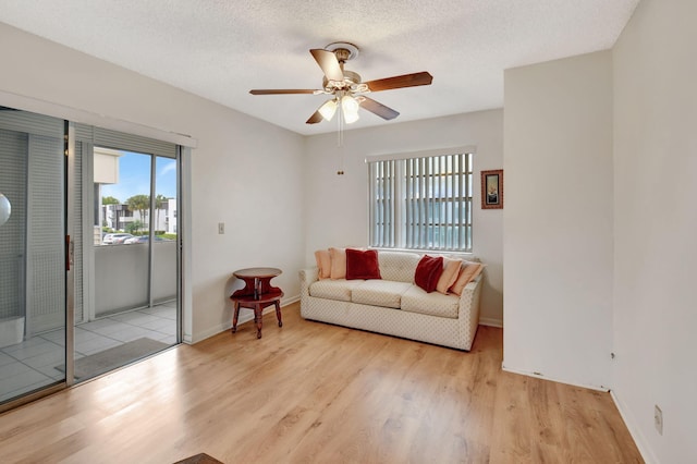 living area featuring baseboards, a textured ceiling, a ceiling fan, and wood finished floors