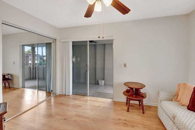 living area featuring baseboards, a ceiling fan, and wood finished floors