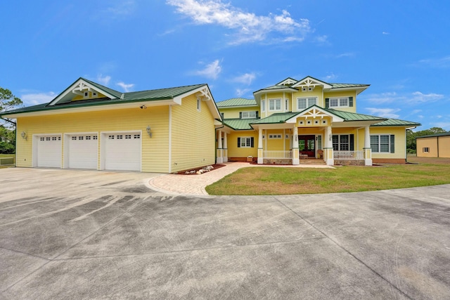 view of front of property with concrete driveway, metal roof, a standing seam roof, covered porch, and a front yard