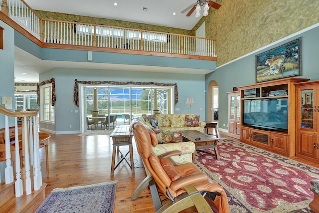 living area featuring arched walkways, a towering ceiling, light wood-style floors, a ceiling fan, and baseboards