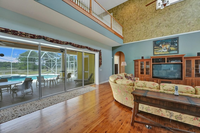 living room with arched walkways, a towering ceiling, a sunroom, ceiling fan, and wood finished floors