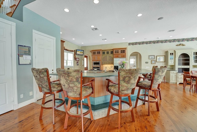 kitchen featuring visible vents, arched walkways, stainless steel microwave, light wood-style floors, and a kitchen bar