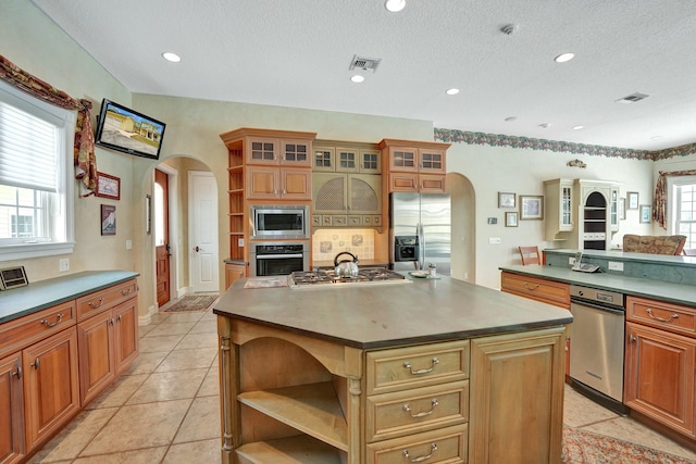 kitchen with arched walkways, a kitchen island, glass insert cabinets, appliances with stainless steel finishes, and open shelves