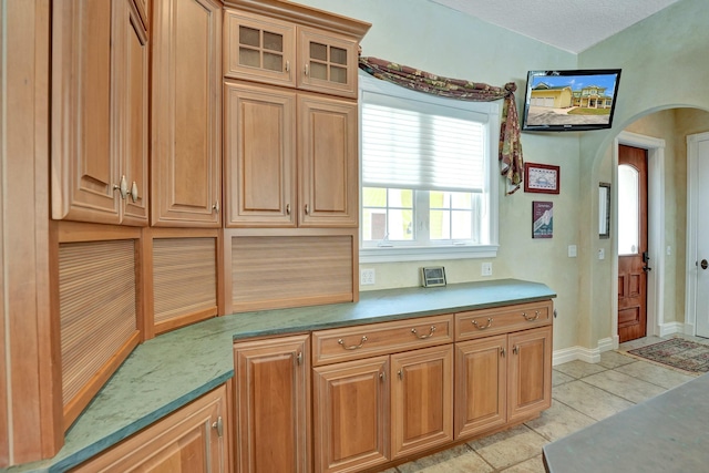 kitchen with glass insert cabinets, arched walkways, light countertops, and light tile patterned flooring