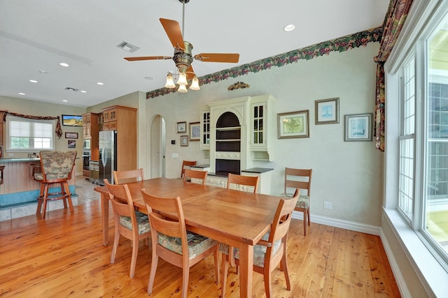 dining area featuring arched walkways, light wood finished floors, visible vents, a ceiling fan, and baseboards