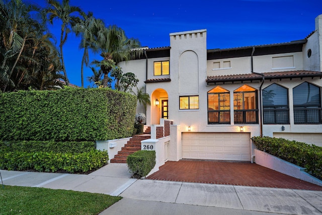 mediterranean / spanish home with a tile roof, stairway, an attached garage, decorative driveway, and stucco siding