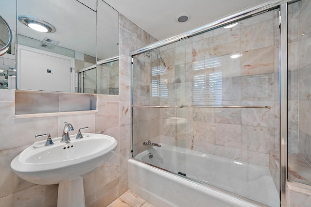 bathroom featuring tile walls, combined bath / shower with glass door, a sink, and visible vents