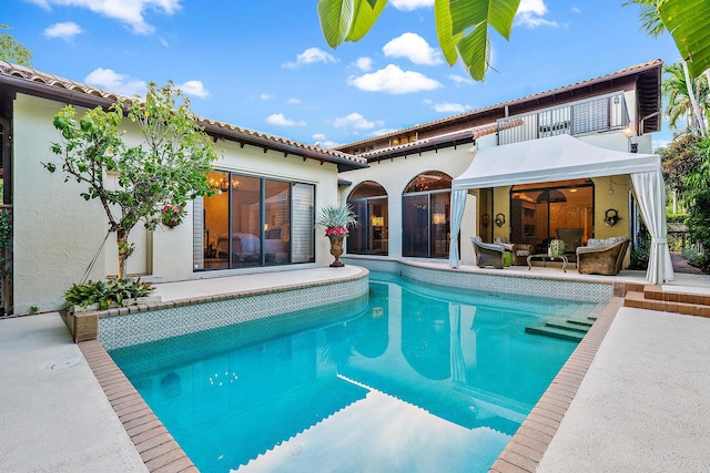 rear view of house with a patio, stucco siding, a balcony, and an outdoor pool