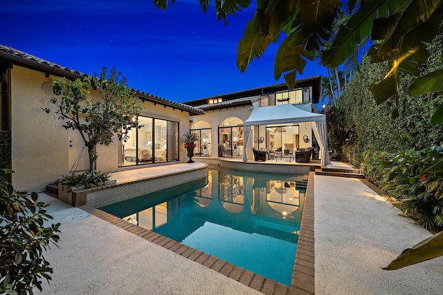 pool at night with a patio area and an outdoor pool