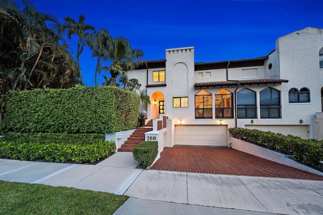 view of front of house with decorative driveway, a tiled roof, an attached garage, and stucco siding