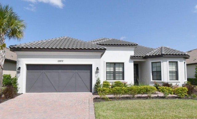 mediterranean / spanish home featuring decorative driveway, a tiled roof, an attached garage, and stucco siding