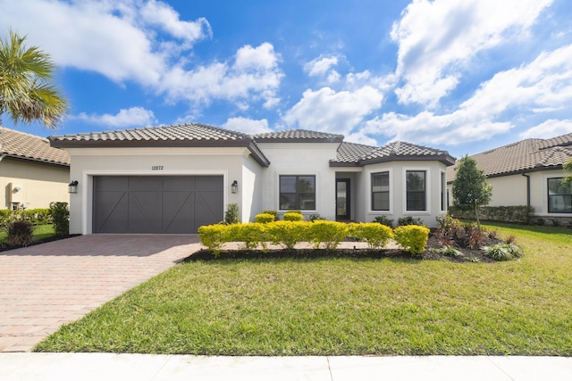 mediterranean / spanish-style house with an attached garage, a tile roof, decorative driveway, stucco siding, and a front lawn