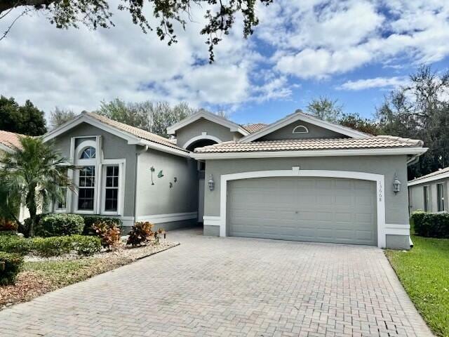 single story home with a garage, decorative driveway, a tile roof, and stucco siding