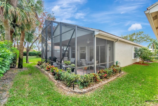 rear view of property featuring stucco siding, a ceiling fan, and a yard