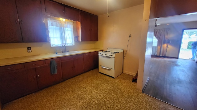 kitchen with white range with gas stovetop, baseboards, light countertops, light floors, and a sink