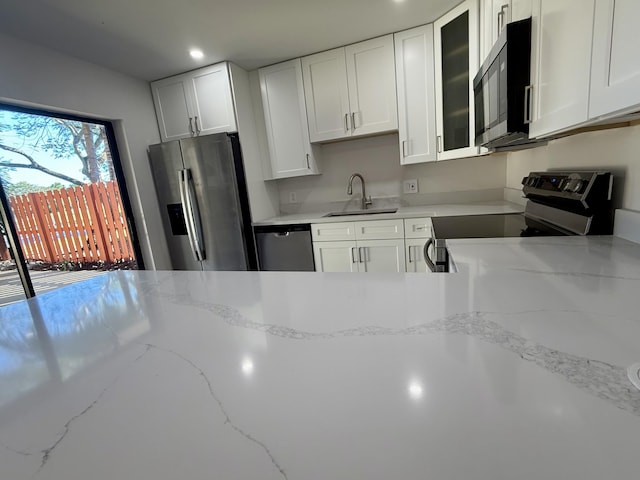 kitchen featuring white cabinets, glass insert cabinets, light stone counters, appliances with stainless steel finishes, and a sink