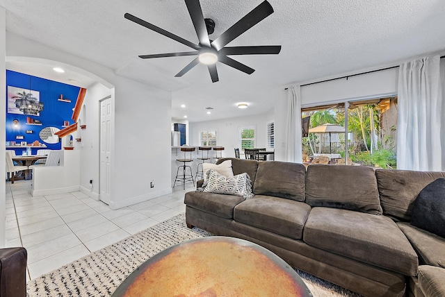 living room featuring light tile patterned floors, arched walkways, baseboards, a ceiling fan, and a textured ceiling