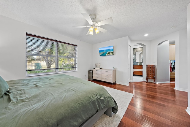 bedroom with baseboards, arched walkways, wood-type flooring, ceiling fan, and a textured ceiling