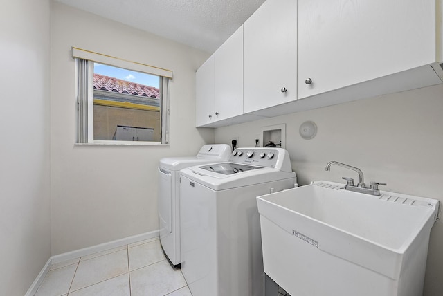 clothes washing area with light tile patterned floors, a sink, baseboards, independent washer and dryer, and cabinet space