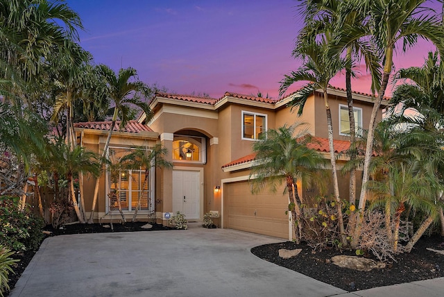 mediterranean / spanish-style home featuring a garage, concrete driveway, a tiled roof, and stucco siding