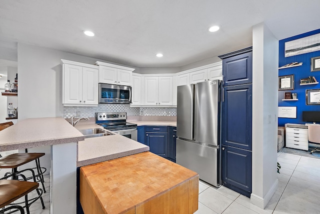 kitchen with stainless steel appliances, a peninsula, a sink, white cabinets, and light countertops