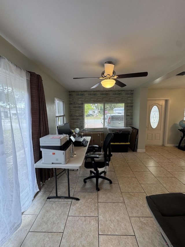 office space with a ceiling fan, visible vents, light tile patterned floors, and brick wall